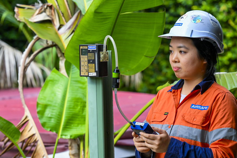 Airsafe consultant using a digital rotameter to check the flow rate of a static asbestos air monitoring pump on site