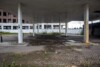 Disused service station forecourt with weathered canopy and overgrown paving