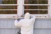 A house painter in a hazmat suit scrapes off dangerous lead paint from a window sill.