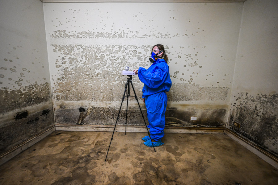 Airsafe consultant taking an air sample with a tripod-mounted pump in a heavily mould-affected room