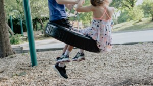 Two children swinging on a tyre swing in a playground.