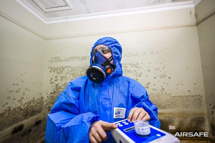 An Airsafe consultant in a respirator taking a mould air sample with a Bio-Pump in a heavily mould-affected room