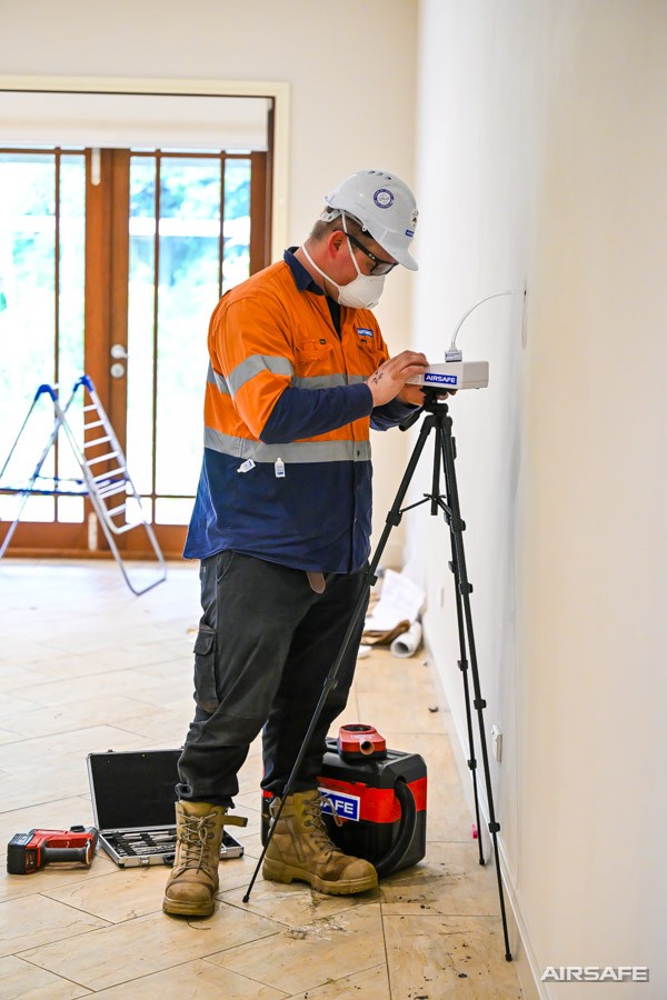 Airsafe consultant setting up tripod-mounted air sampling equipment in an empty room