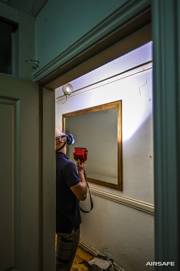 An Airsafe consultant in a respirator examining the ceiling of a water-damaged room