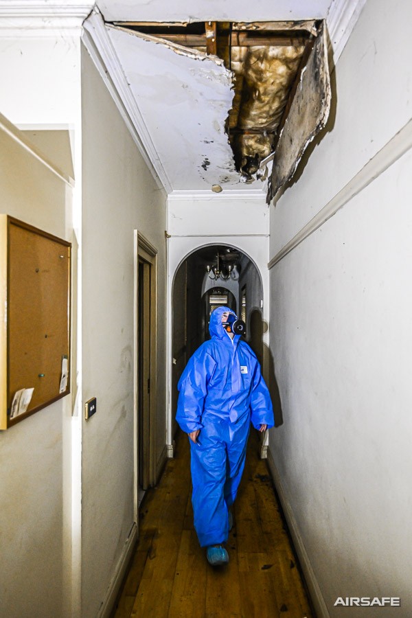 An Airsafe consultant in protective coveralls walking a hallway beneath a collapsed water-damaged ceiling