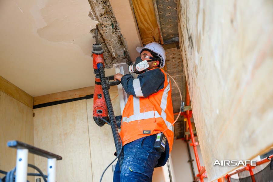 Worker chipping concrete from a ceiling beam while wearing an Airsafe personal silica sampling pump