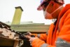Airsafe consultant in a respirator and hard hat taking a sample from the weathered edge of a corrugated asbestos cement roof sheet on an older house