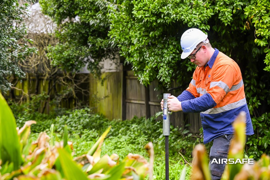 Airsafe consultant taking a soil sample in the overgrown backyard of an older home