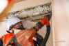 Worker in hard hat, respirator and hi vis chipping concrete from a ceiling slab with on tool dust extraction