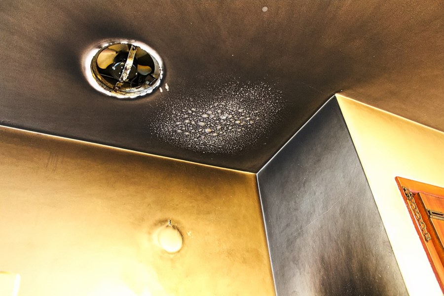 Soot-blackened ceiling and wall around an exhaust fan after a fire